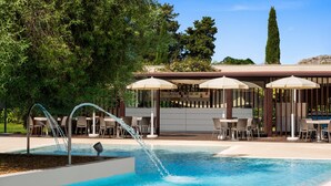 A swimming pool with water features, outdoor seating, and a bar area. - Dolce by Wyndham Siracusa I Monasteri Golf & Spa (Syracuse)