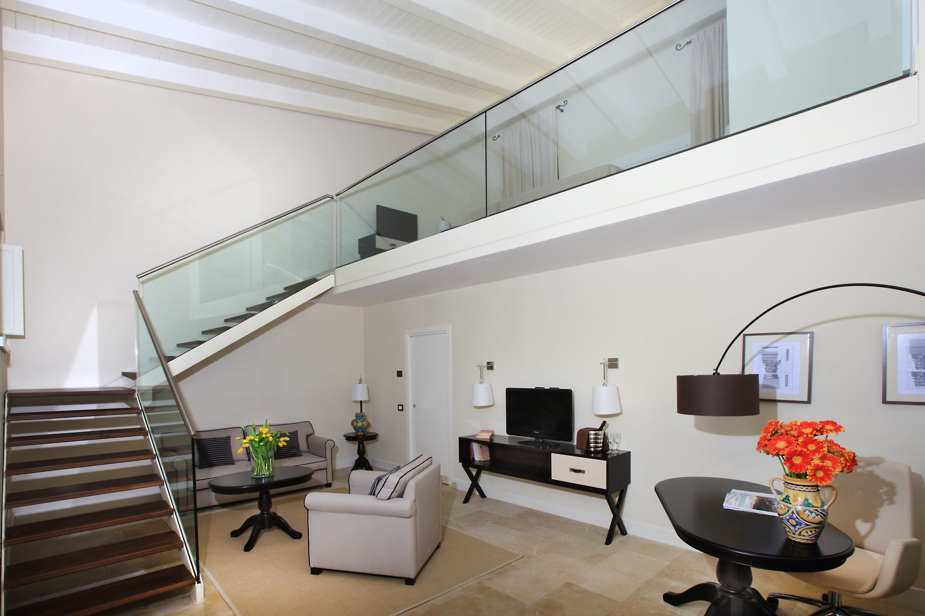 A modern living room with a staircase, a sofa, a coffee table, a TV, and a vase with flowers.