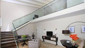 A modern living room with a staircase, a sofa, a coffee table, a TV, and a vase with flowers.