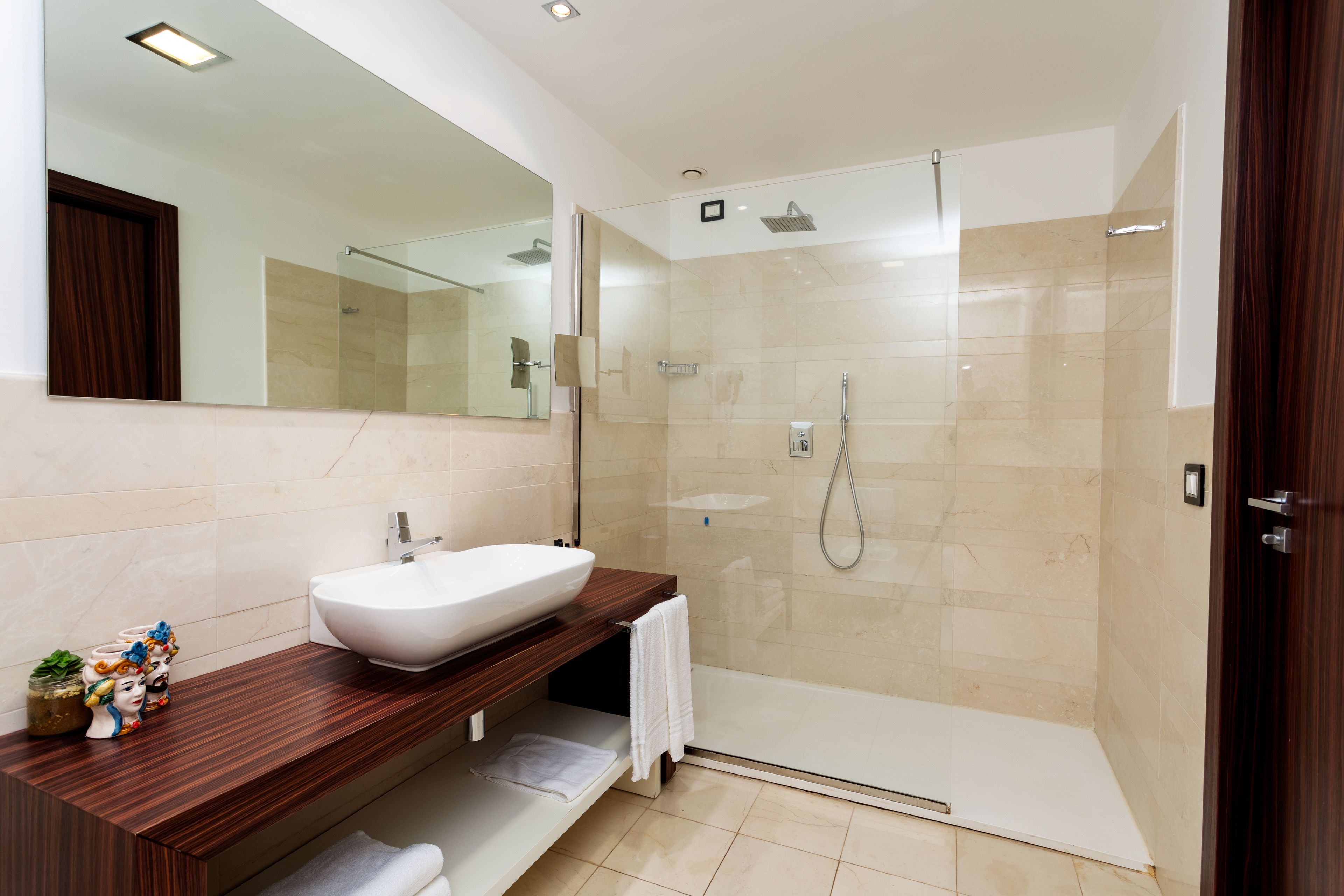 A modern bathroom with a large mirror, a wooden vanity, a white sink, and a glass-enclosed shower.