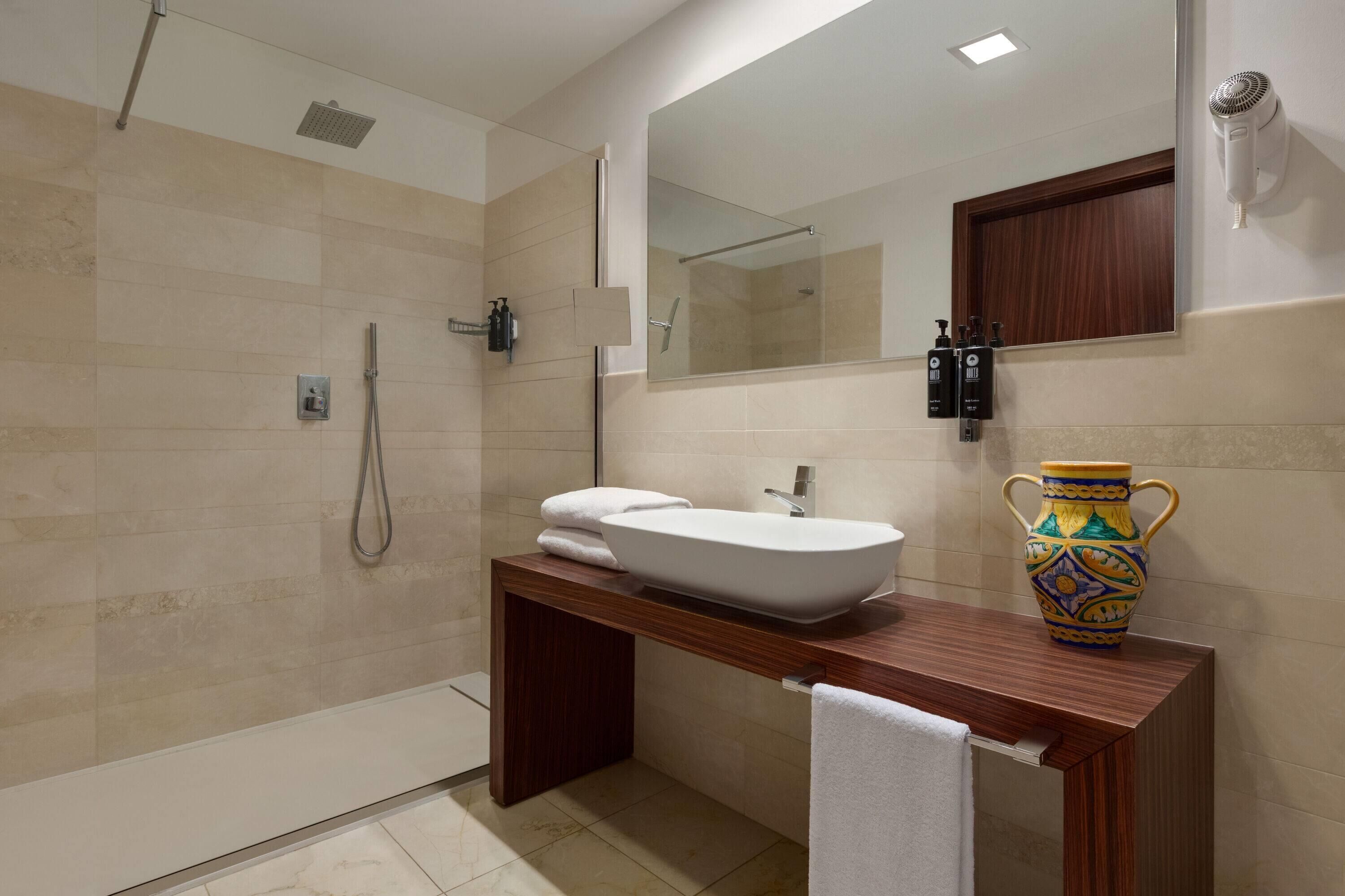 A modern bathroom with a large sink, a shower, and a mirror.