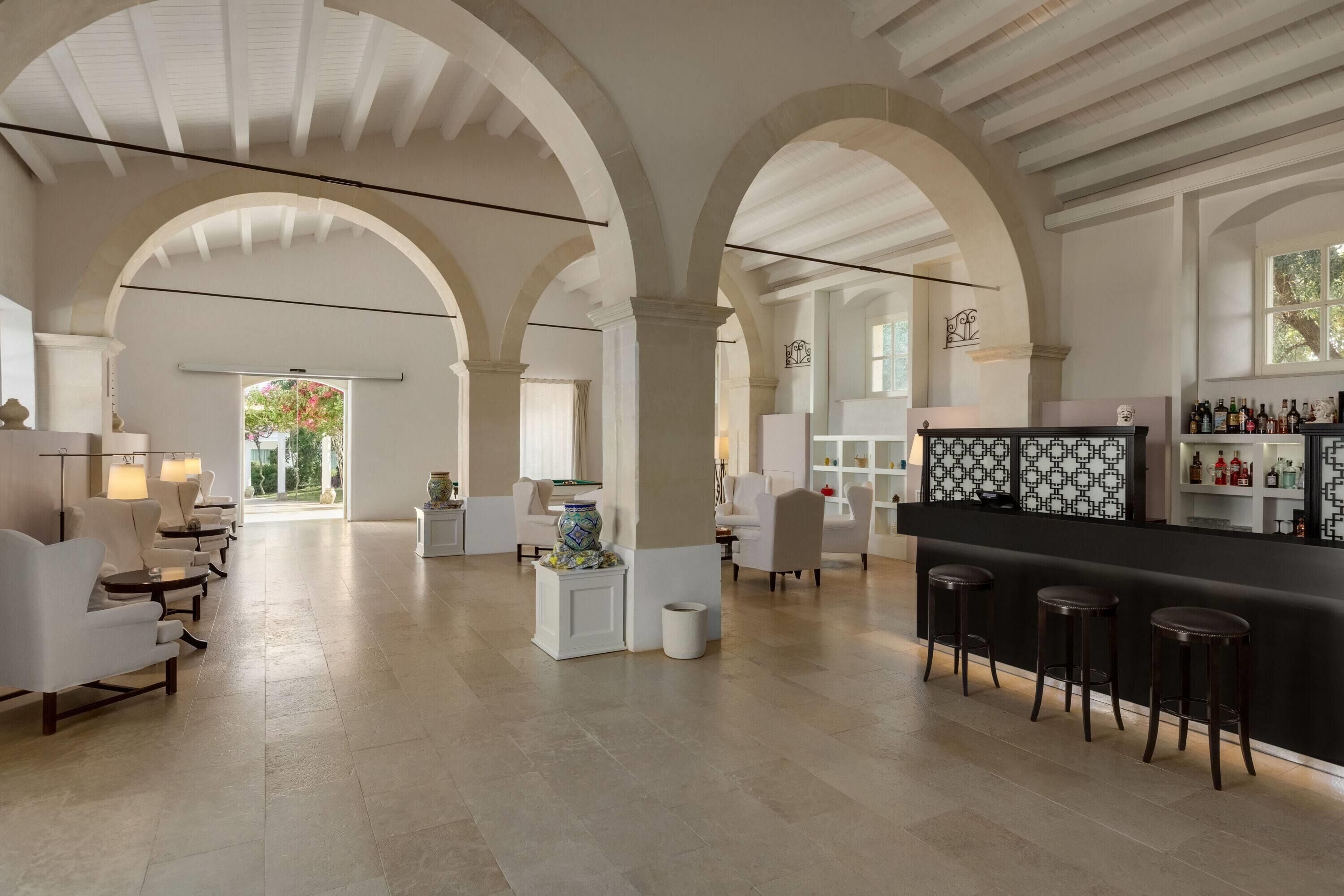 A spacious lobby with high arched ceilings, a central bar area with stools, and a seating area with sofas and tables.