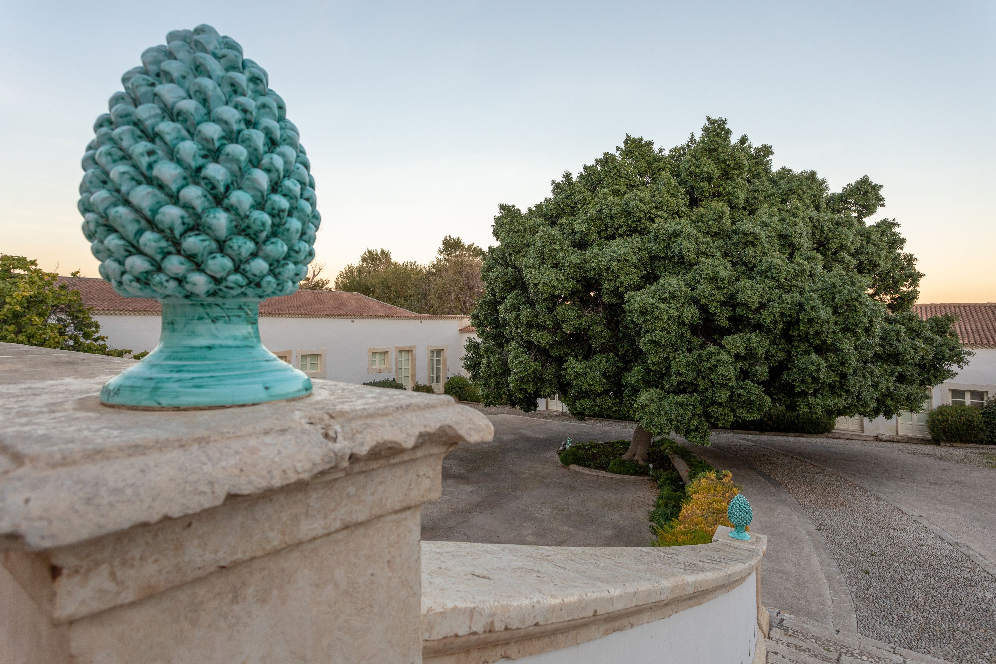 Una barandilla de piedra con una urna decorativa y un gran árbol en una zona residencial.