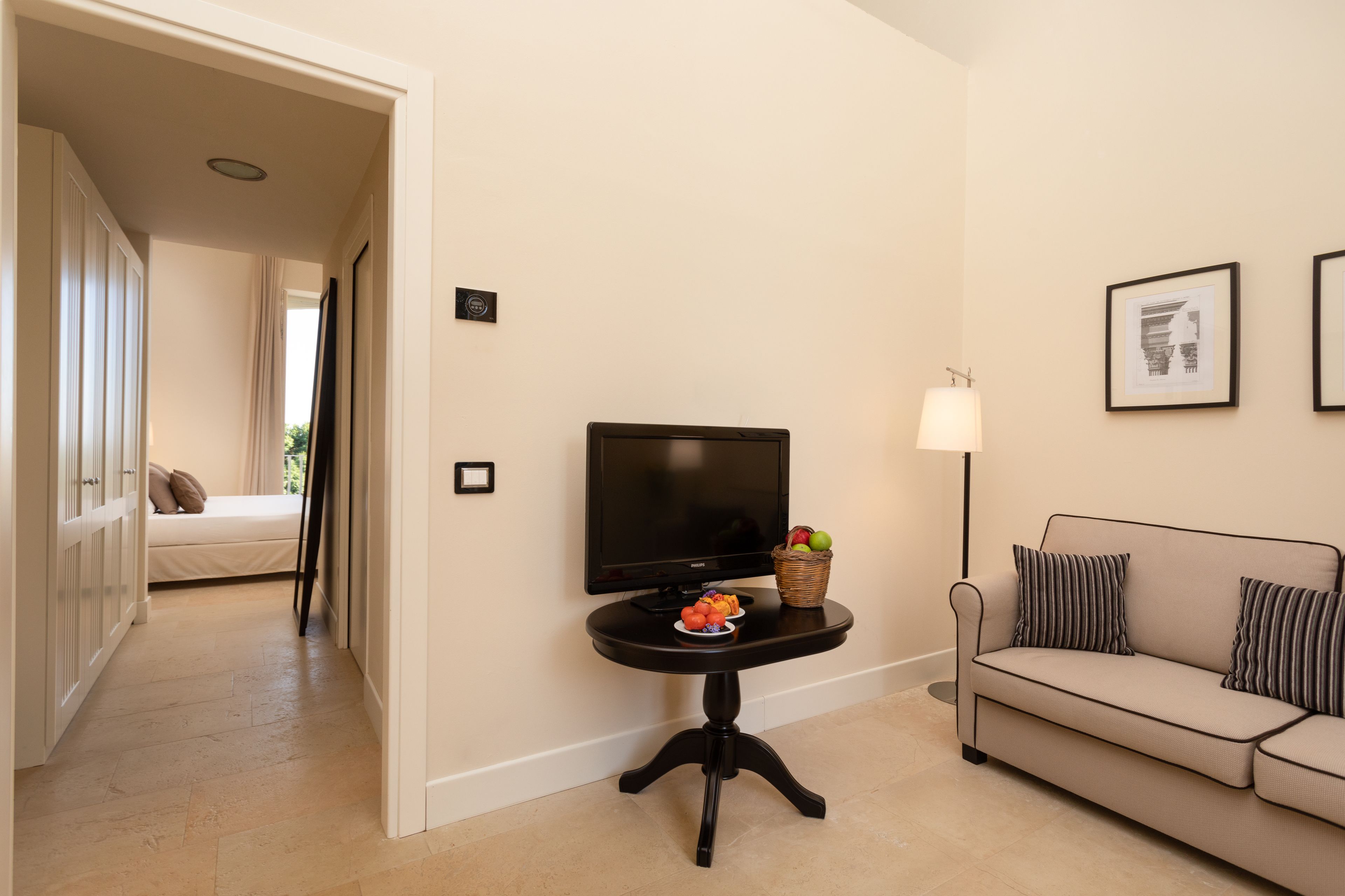 A living room with a sofa, a television on a stand, a small table with fruit, and a lamp.