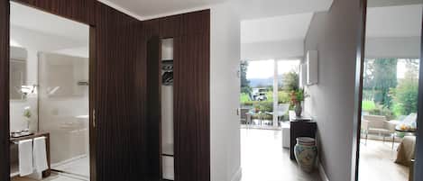 Un interior moderno con suelo de madera, una puerta de cristal que da a un baño y vistas a un patio con mobiliario exterior.
