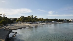 A waterfront promenade with clear water, a stone walkway, and a row of beach umbrellas. - Dolce by Wyndham Siracusa I Monasteri Golf & Spa (Syracuse)