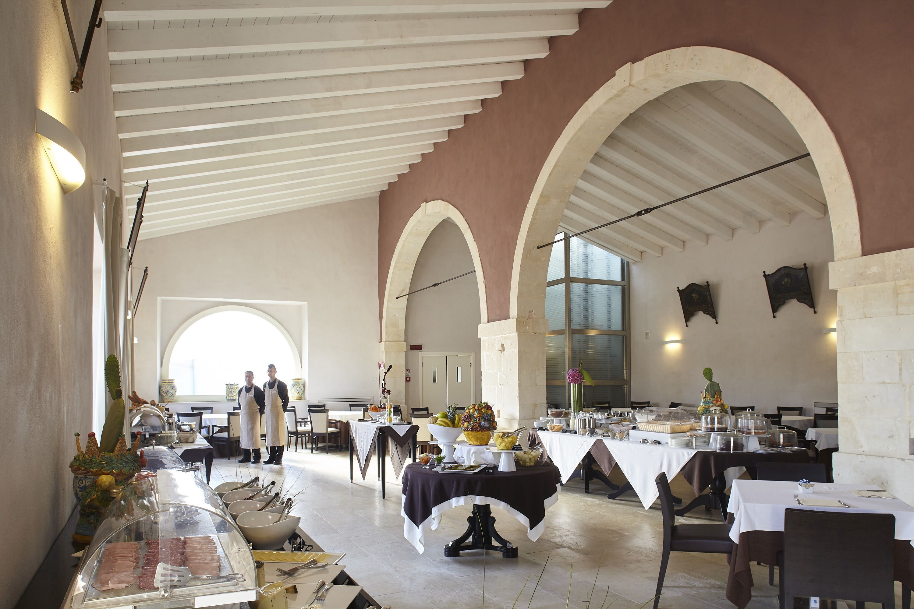Ein geräumiger Speisebereich mit mehreren Tischen, einem zentralen Buffet und einem großen Bogenfenster, das für natürliches Licht sorgt.