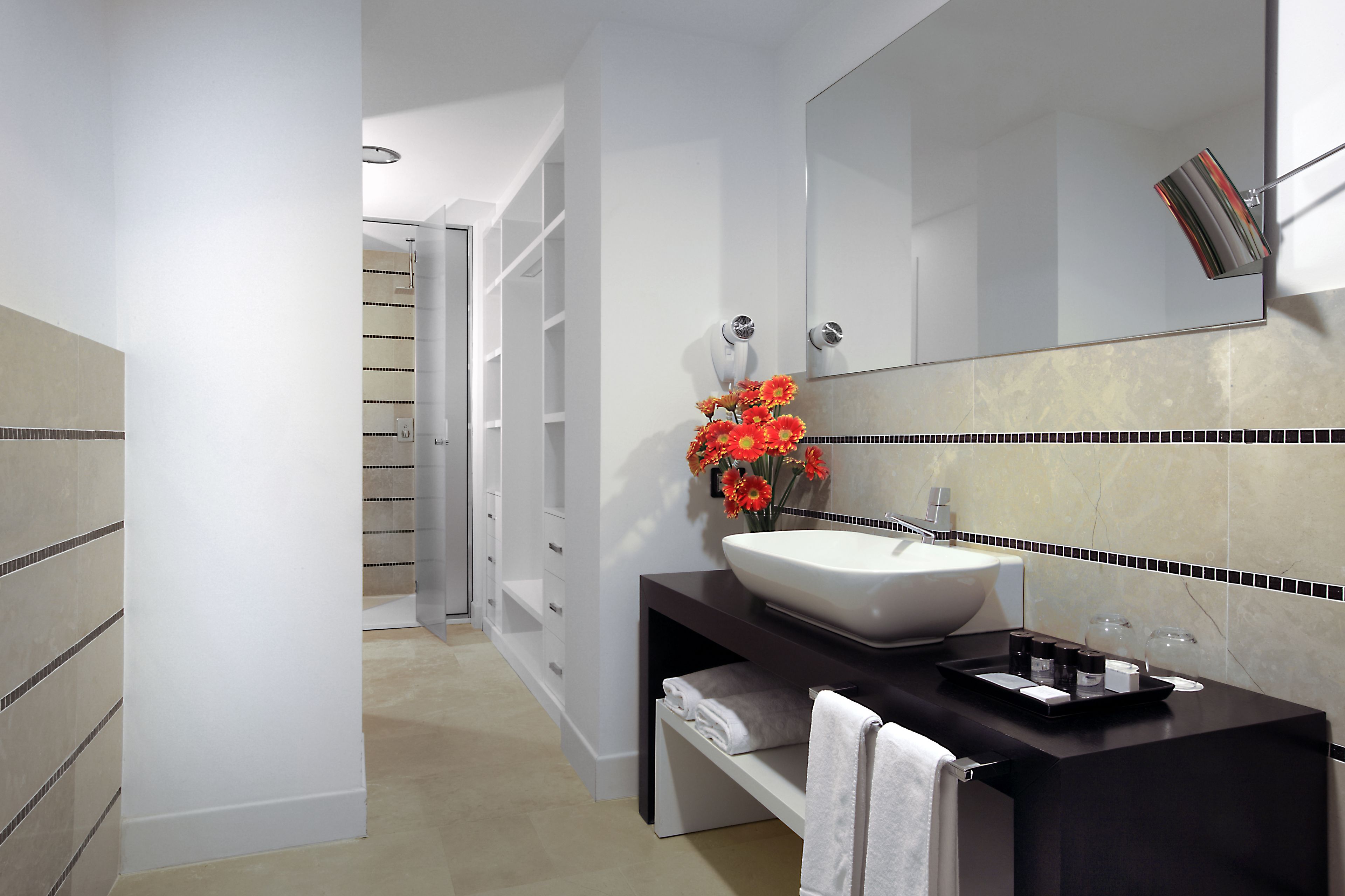 A modern bathroom with a large mirror, white sink, and a vase of red flowers.