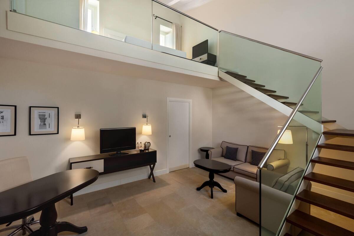 Ein modernes Wohnzimmer mit einer Glaskonstruktion als Treppe, einem Flachbildfernseher, einem Sofa und einem Esstisch.