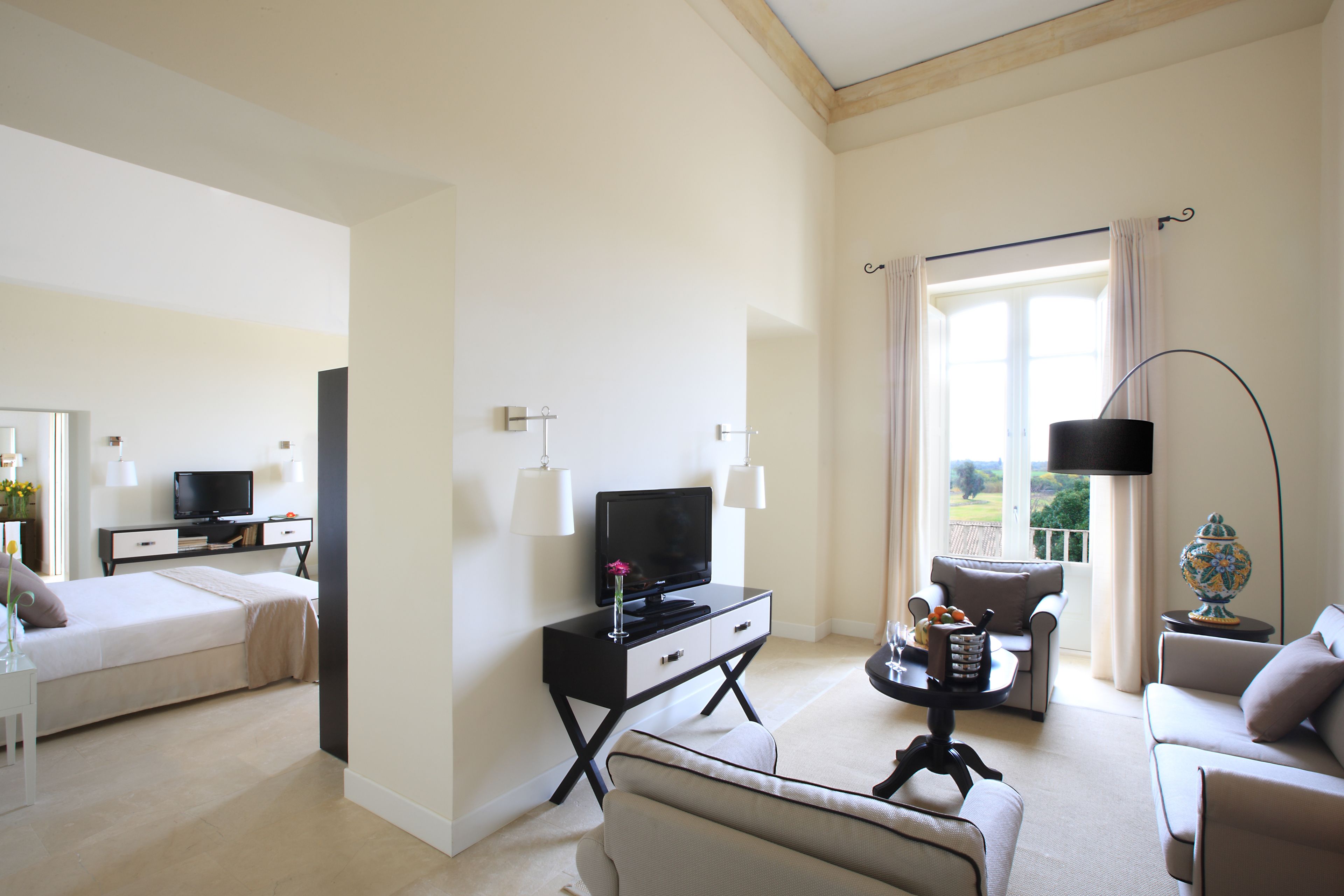 Una camera d'hotel moderna con un letto, una TV, una scrivania con una lampada, un divano e vista sull'esterno.