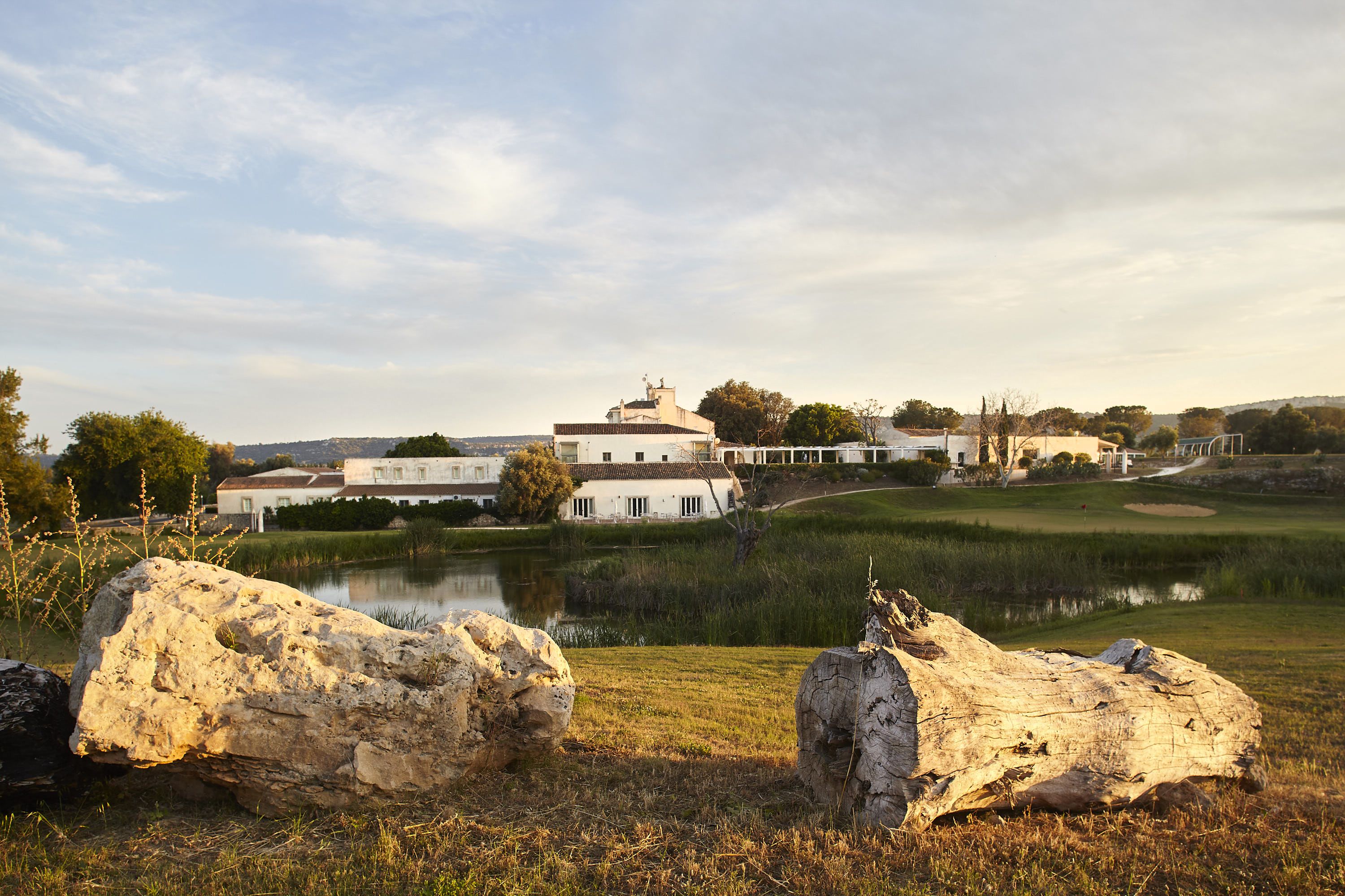 A large building with multiple white structures, a pond, and large rocks in the foreground.