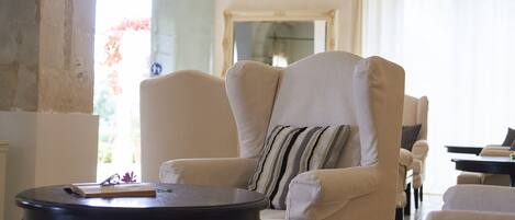 Een woonkamer met een beige fauteuil, een ronde zwarte tafel en een gestreept kussen.