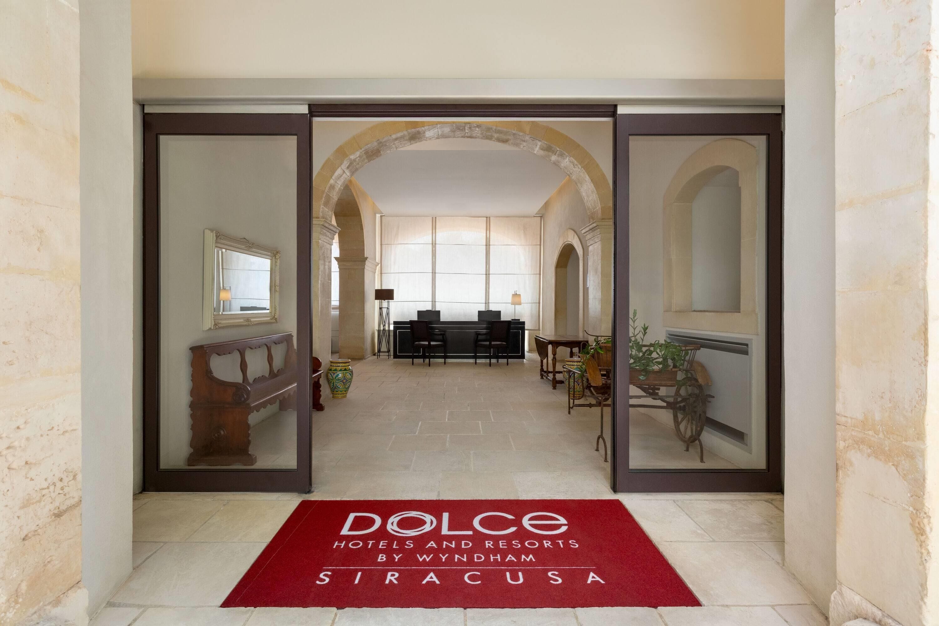 A hotel corridor with a red carpet leading to a reception area.