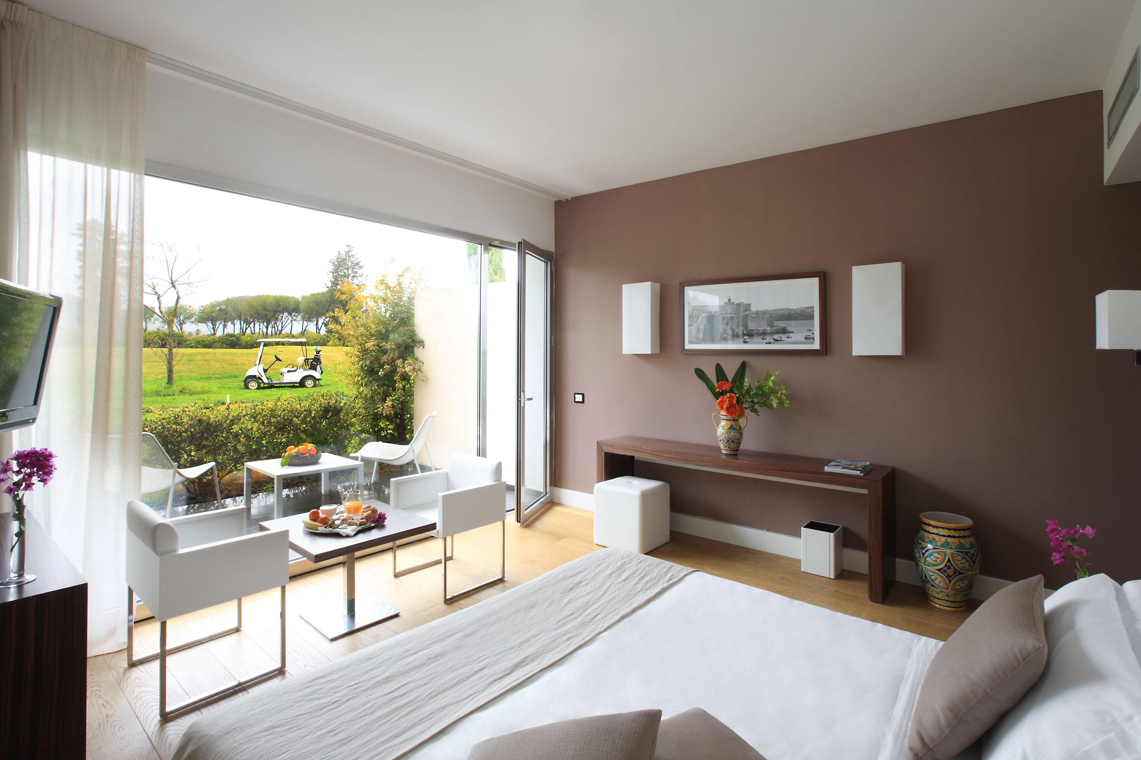 Una habitación de hotel moderna con una cama grande, un escritorio, una silla y vistas a un campo de golf.