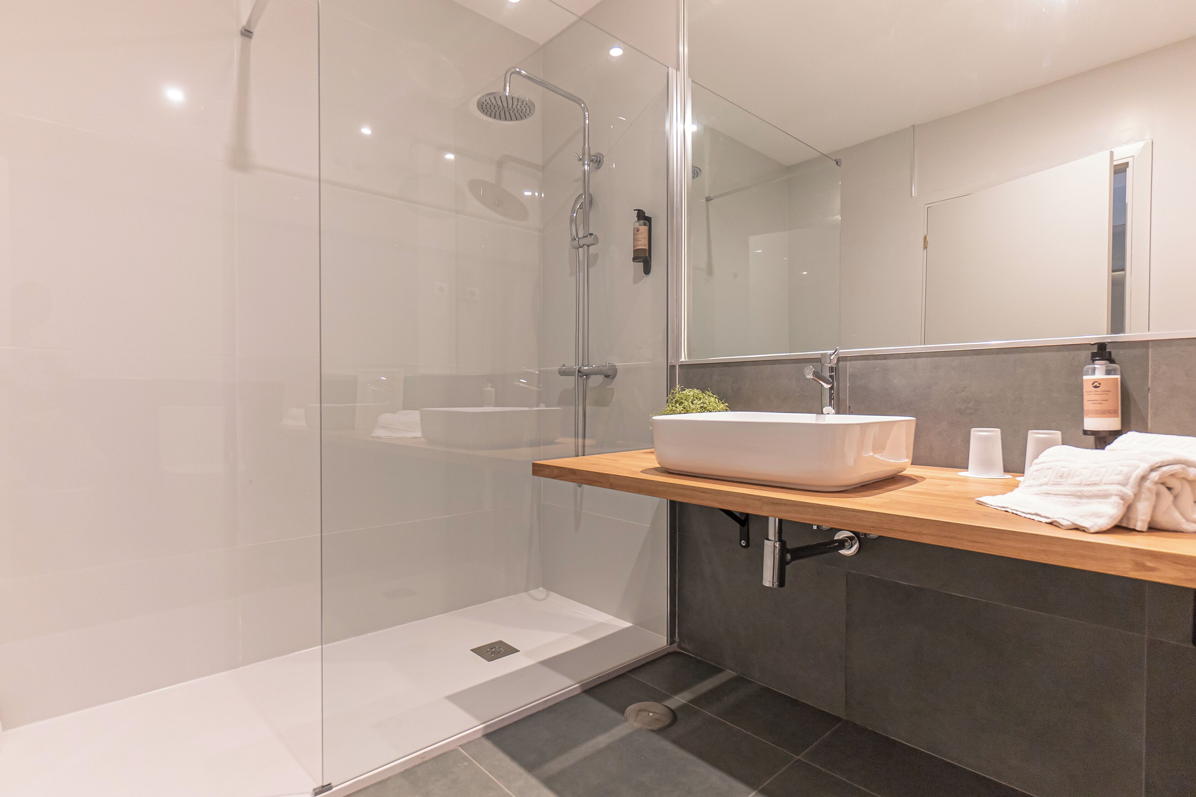 A modern bathroom with a glass-enclosed shower, a wooden vanity with a sink, and a mirror.