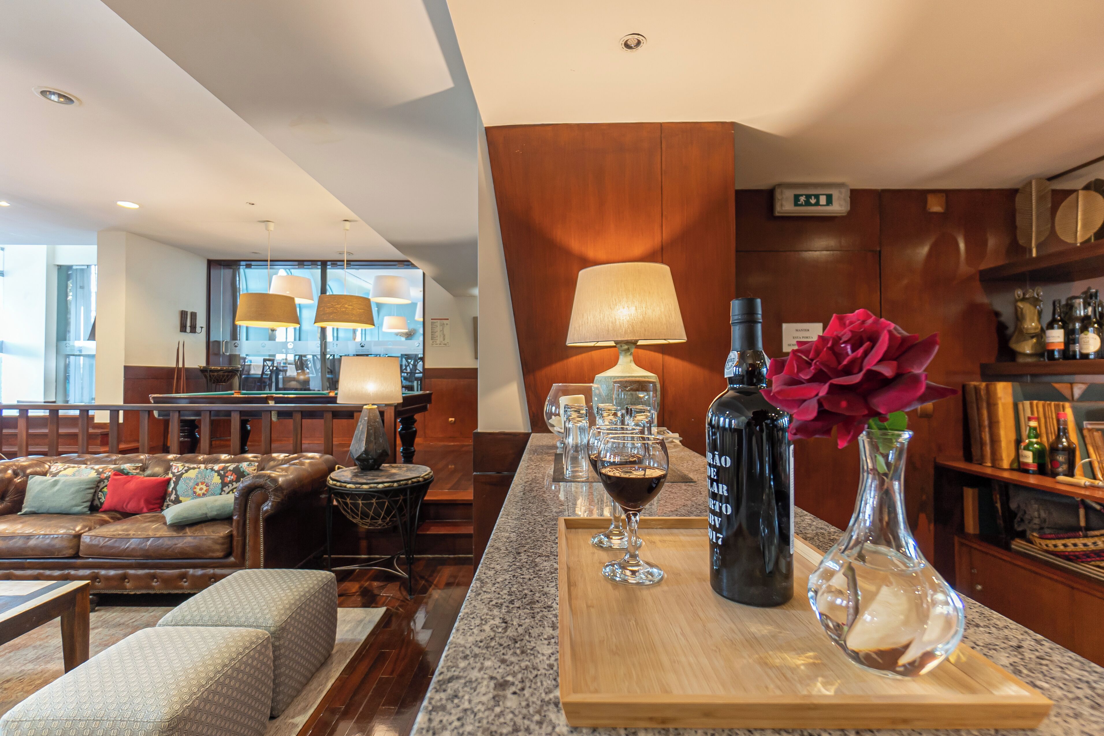Un hall d’hôtel moderne avec un canapé en cuir, une table basse en bois et un coin bar agrémenté d’un verre à vin et d’une bouteille de vin.