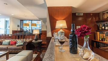 Un hall d’hôtel moderne avec un canapé en cuir, une table basse en bois et un coin bar agrémenté d’un verre à vin et d’une bouteille de vin.