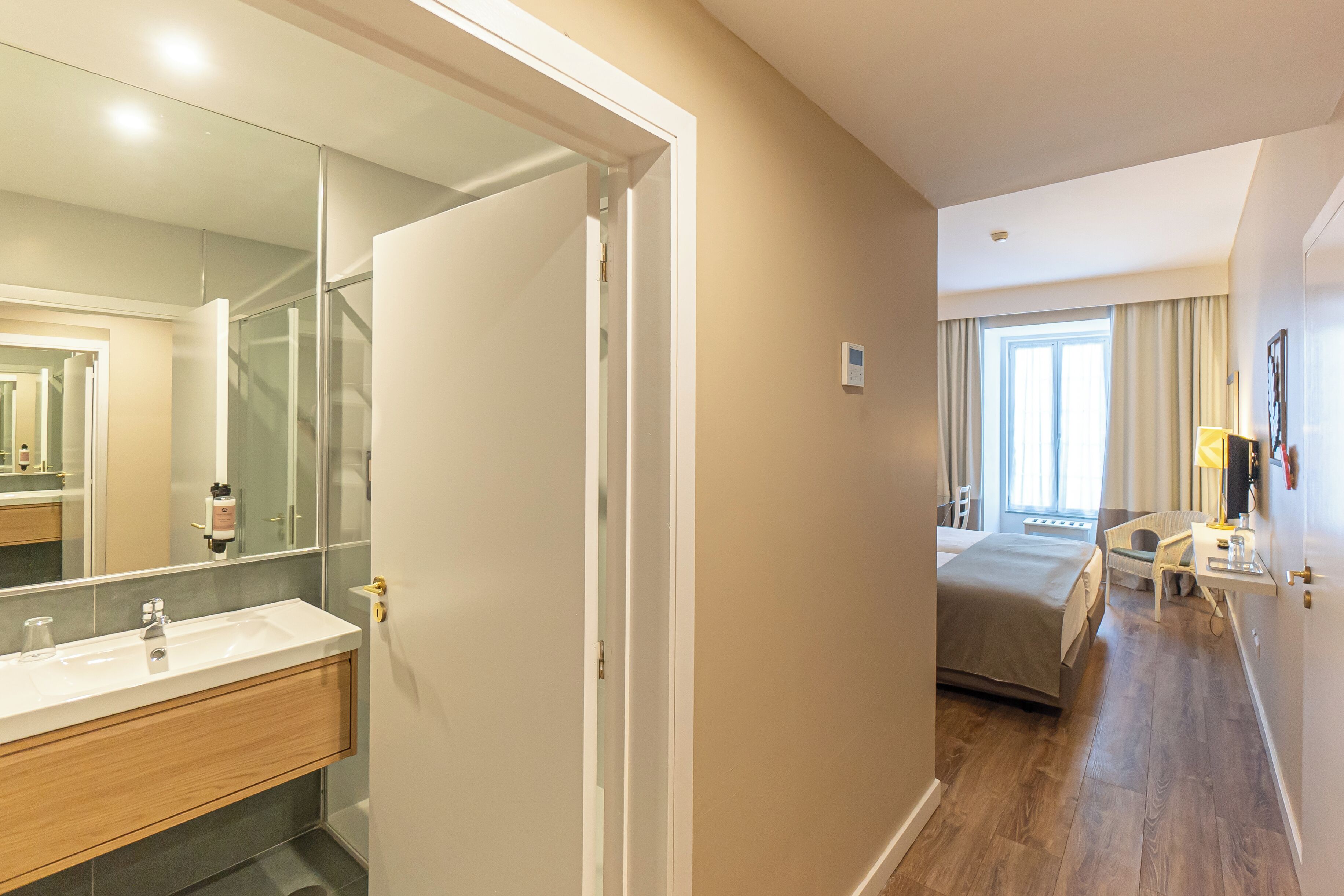 A hotel room with a large mirror, a wooden vanity, a bed, and a desk with a lamp.