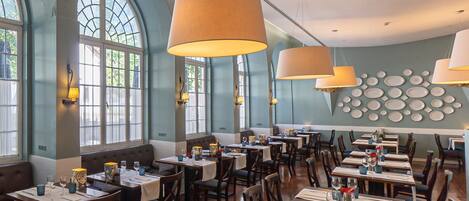 Un restaurante con ventanales altos de arco, mesas de madera y lámparas colgantes.