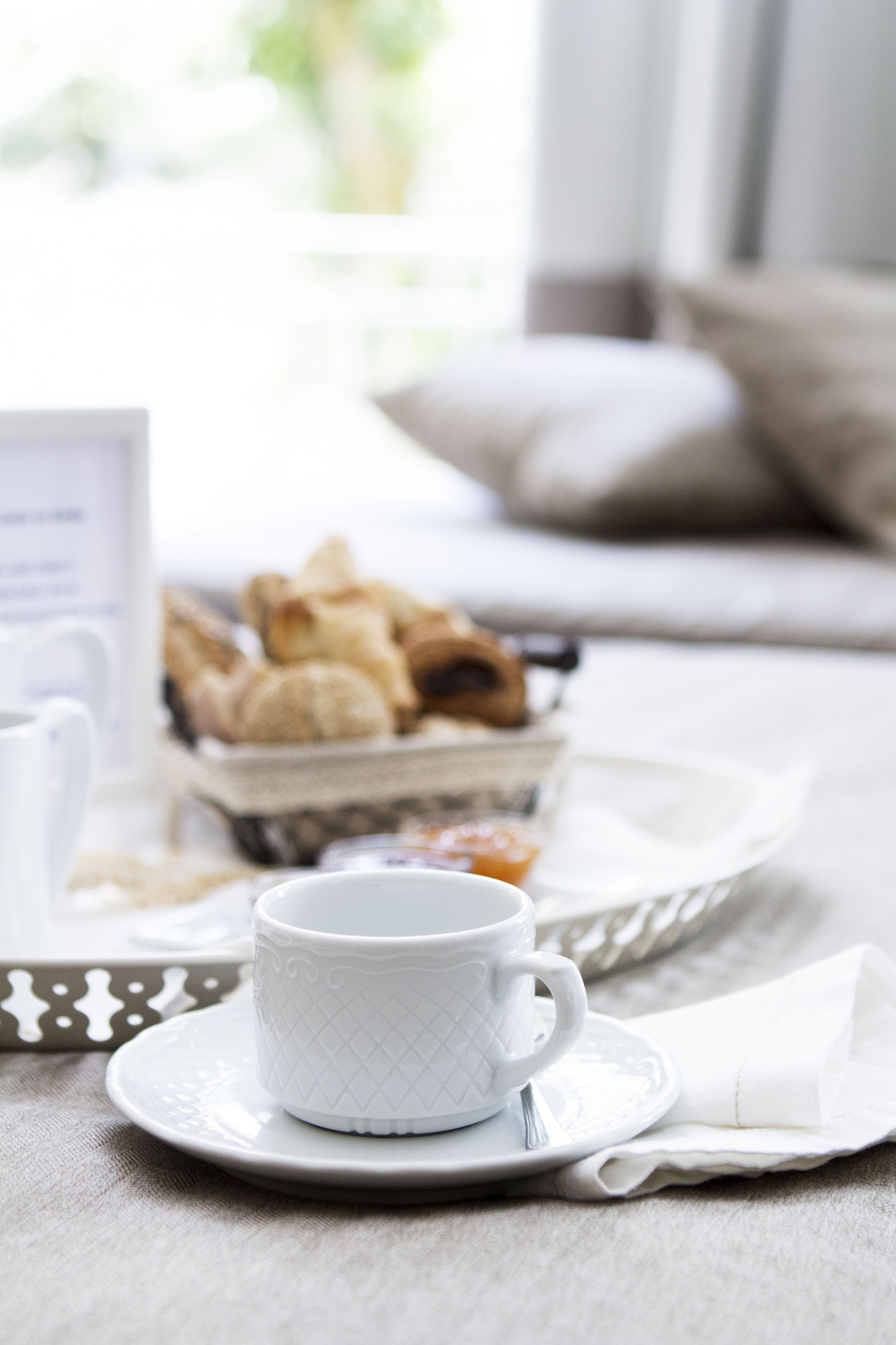 A breakfast setting with a cup and saucer, a tray of pastries, and a napkin on a table.