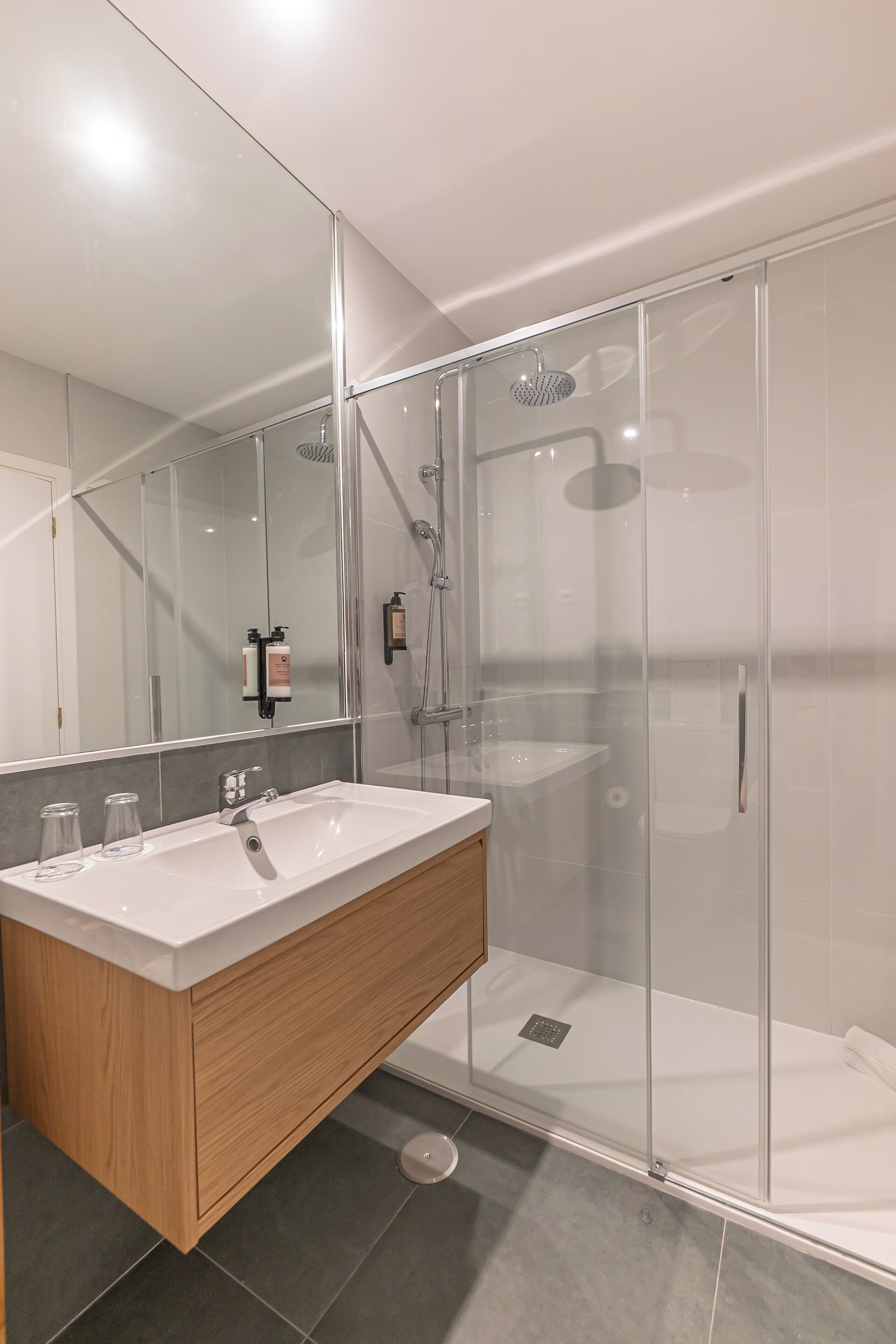 Une salle de bain moderne avec une douche à parois de verre, un grand miroir et un meuble-lavabo en bois.