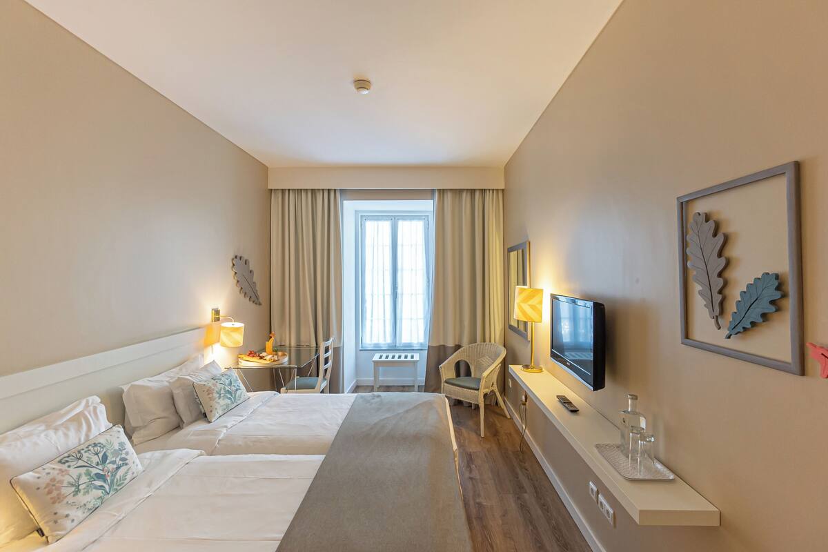 A hotel room with two beds, a television, a desk with a lamp, and a chair.