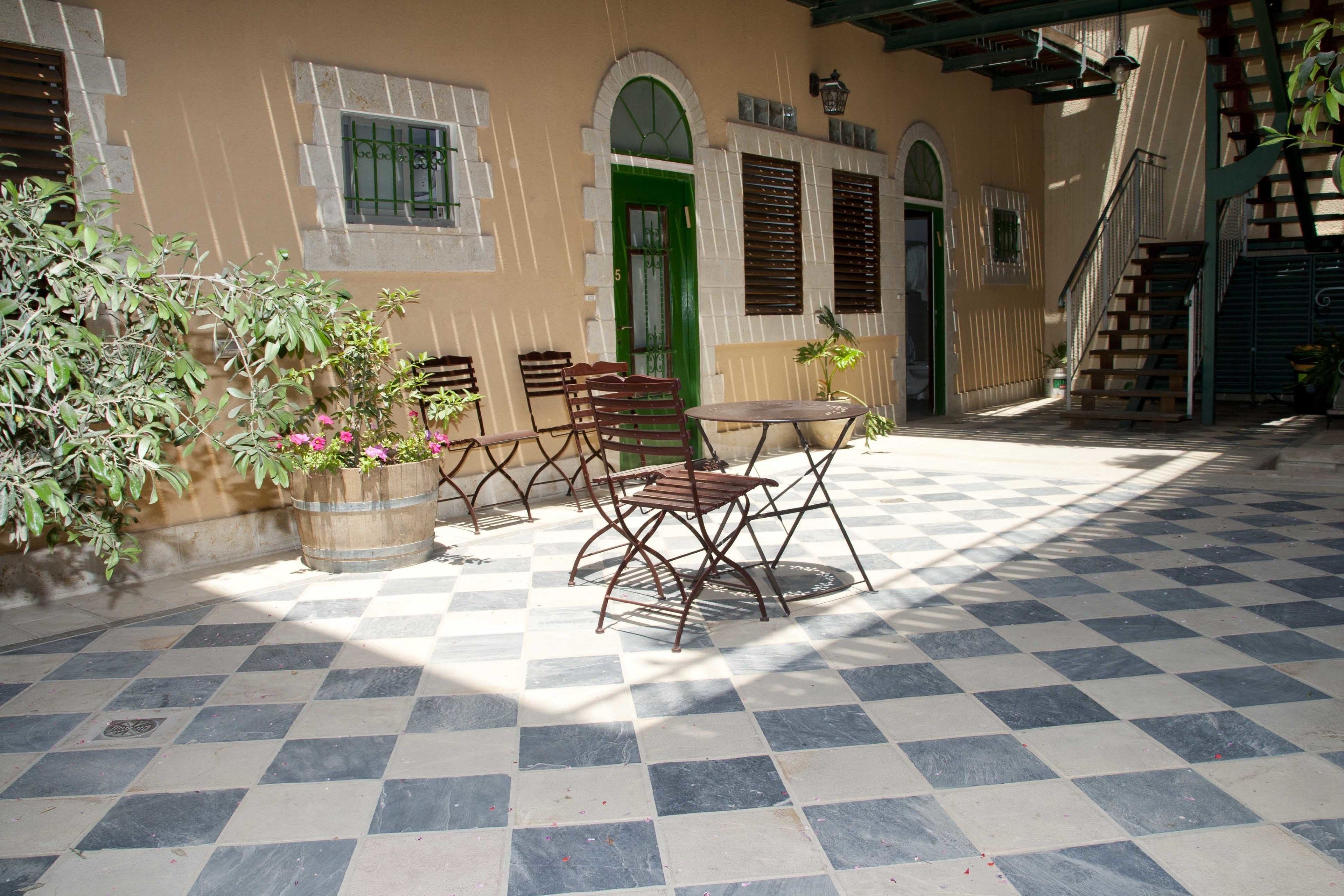 A courtyard with a checkered floor, outdoor seating, and a green door.