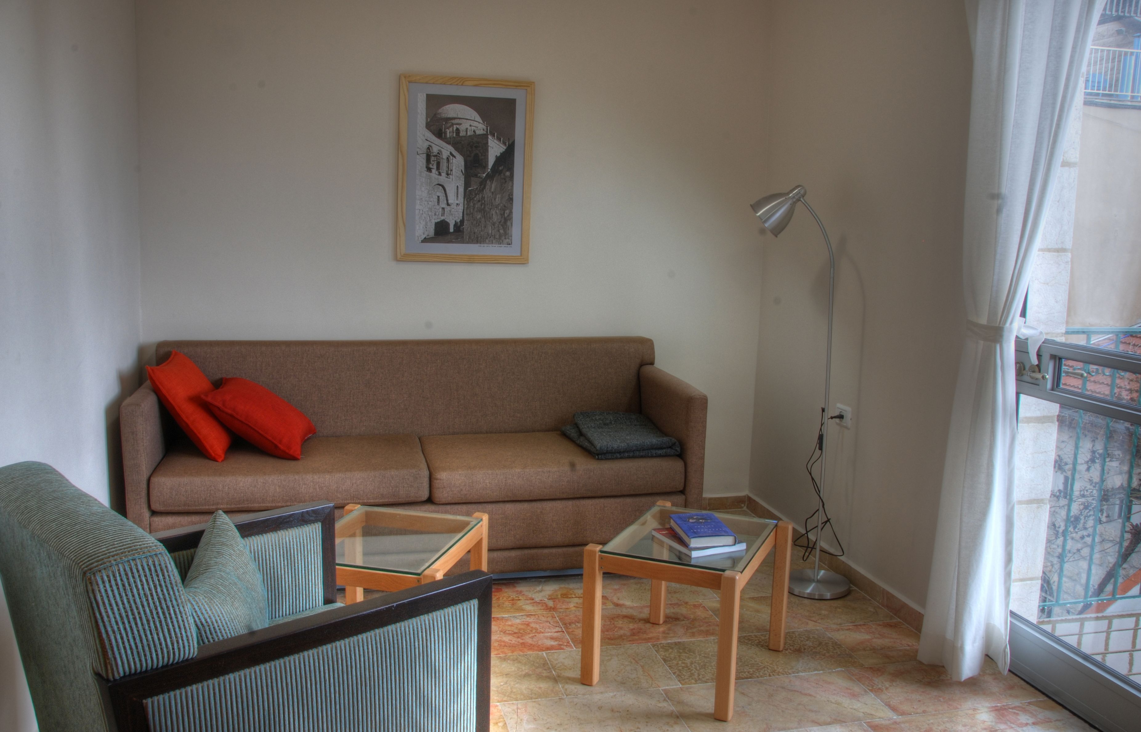 Ein Wohnzimmer mit braunem Sofa, roten und blauen Kissen, einem Glastisch und einem gerahmten Bild an der Wand.