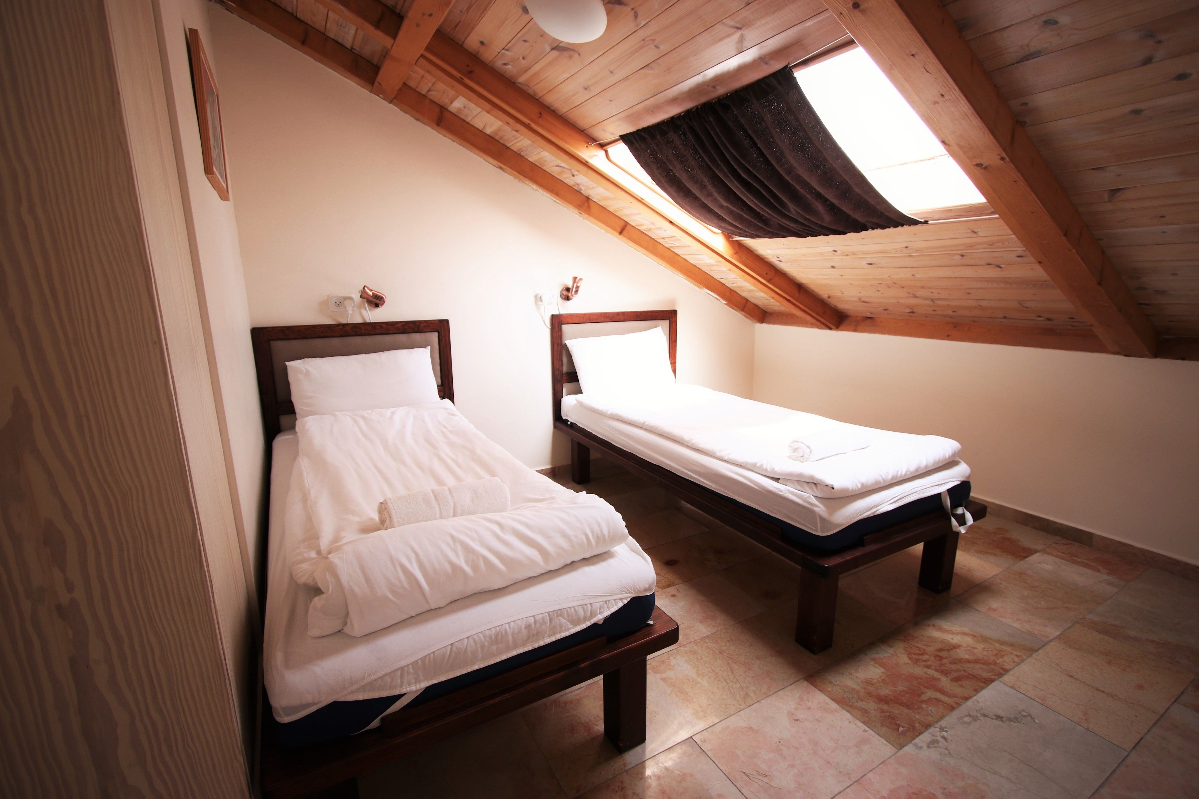 Dos camas individuales en una habitación con techo inclinado y tragaluz.