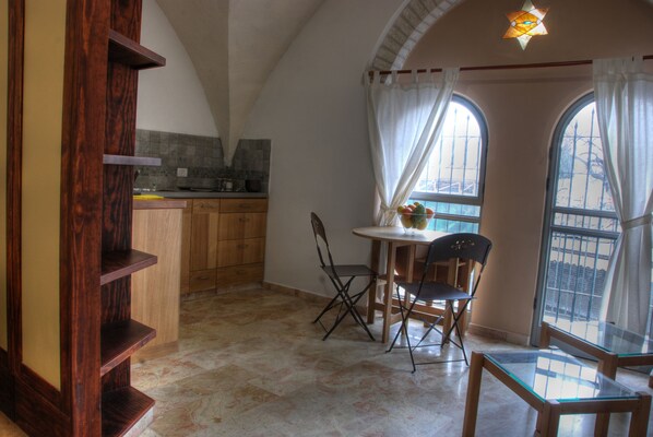 A kitchen with wooden cabinets, a dining table with chairs, and a window with curtains. - The Market Courtyard - Jerusalem Suites (Jerusalem)
