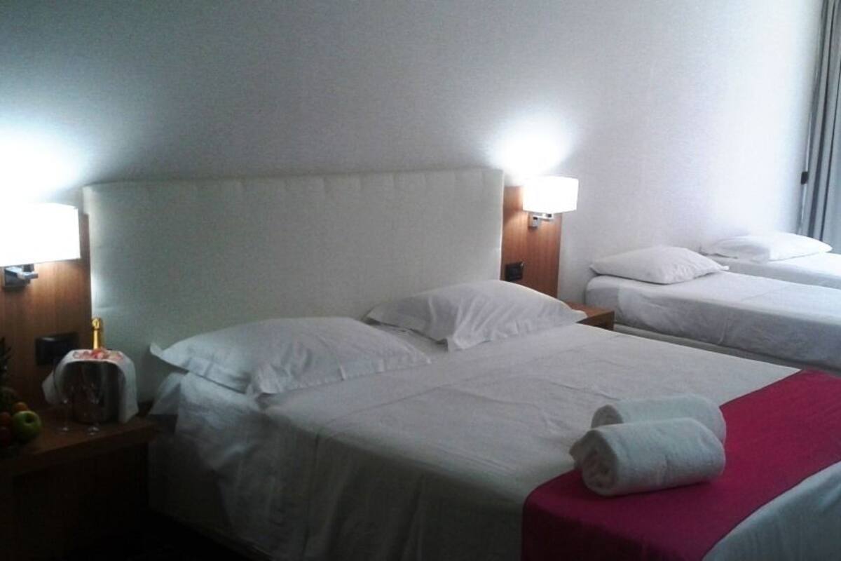 A hotel room with two beds, each with white linens and pillows, a red blanket on one bed, and a fruit bowl on the nightstand.