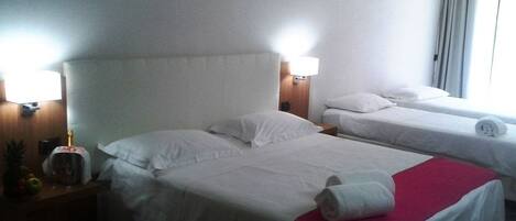 Une chambre d’hôtel avec deux lits, chacun agrémenté de draps et d’oreillers blancs, une couverture rouge sur l’un des lits et un panier de fruits sur la table de chevet.