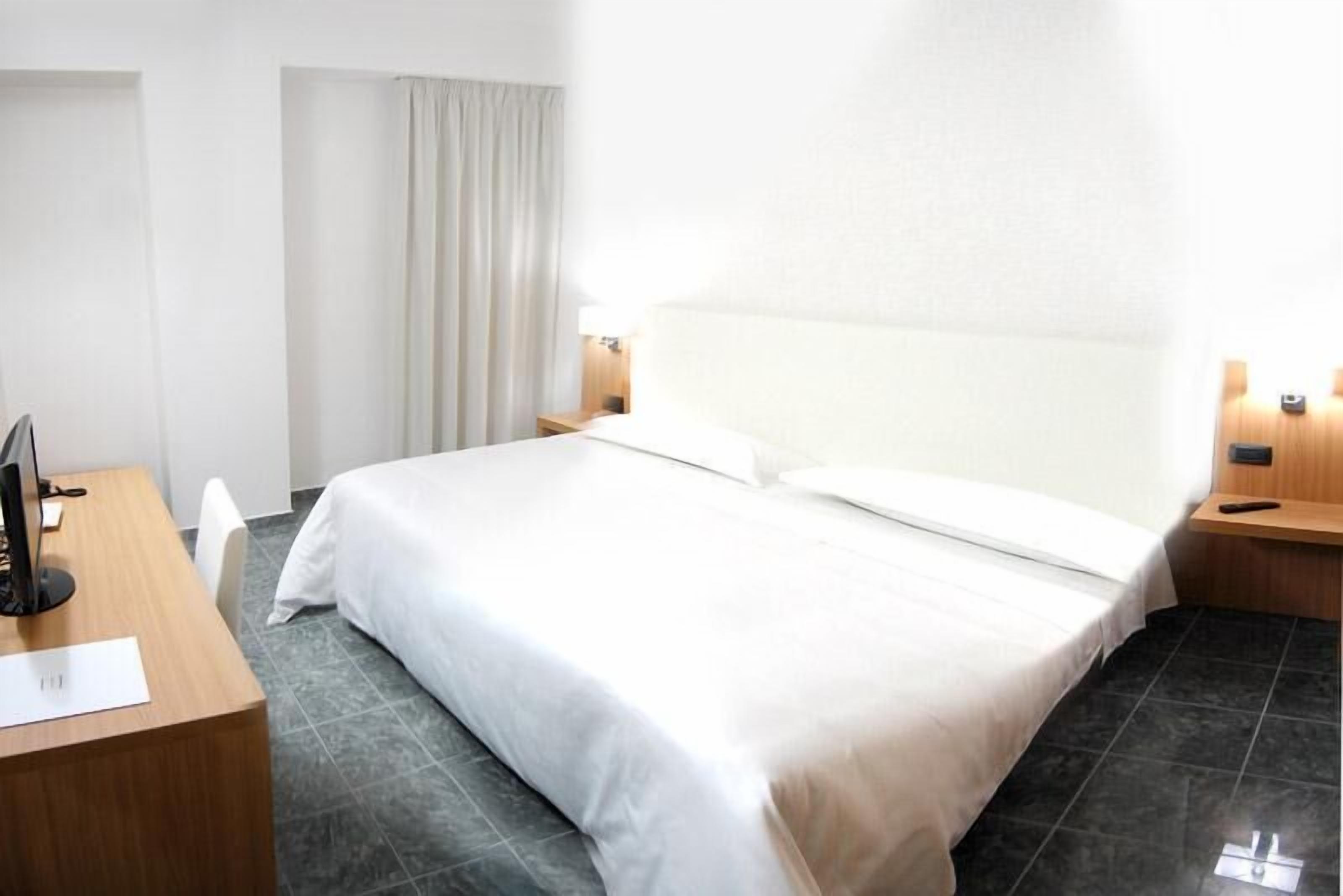 A hotel room with a large bed, a desk with a computer, and a chair.