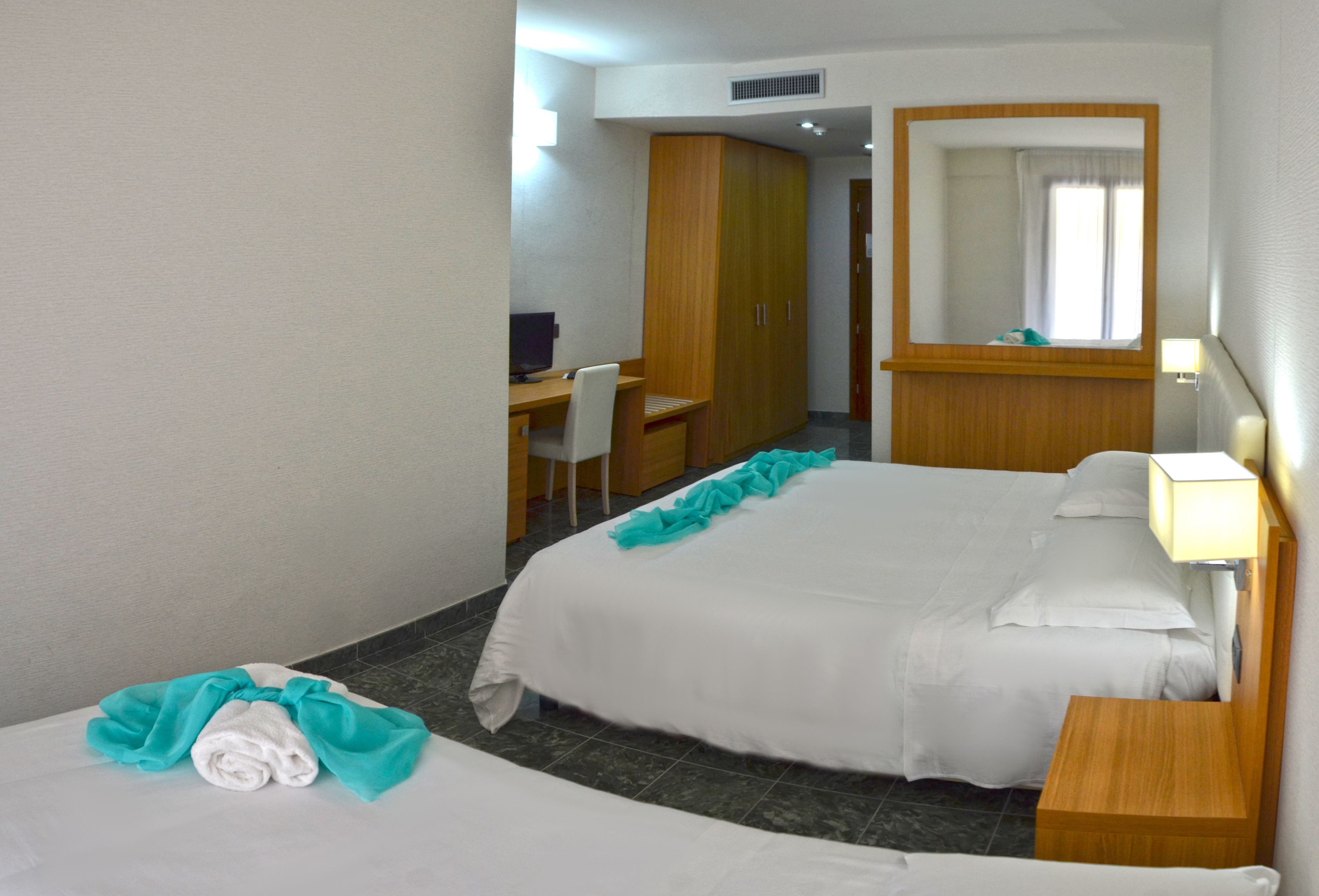 A hotel room with two beds, a desk, a chair, a mirror, and a nightstand.