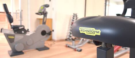 Ein Fitnessraum mit Trainingsgeräten, darunter ein Ergometer und ein Laufband.