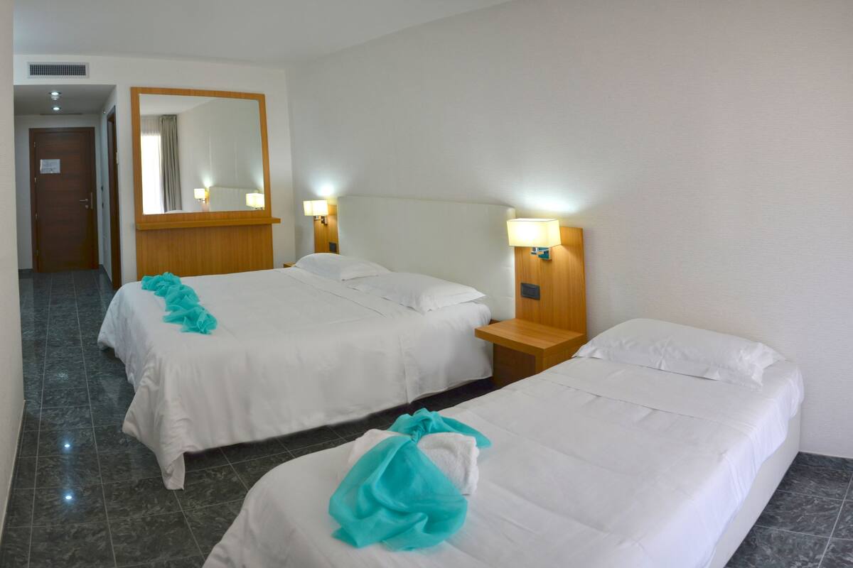 A hotel room with two beds, a wooden headboard, a nightstand with a lamp, and a mirror on the wall.