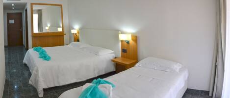 A hotel room with two beds, a wooden headboard, a nightstand with a lamp, and a mirror on the wall.