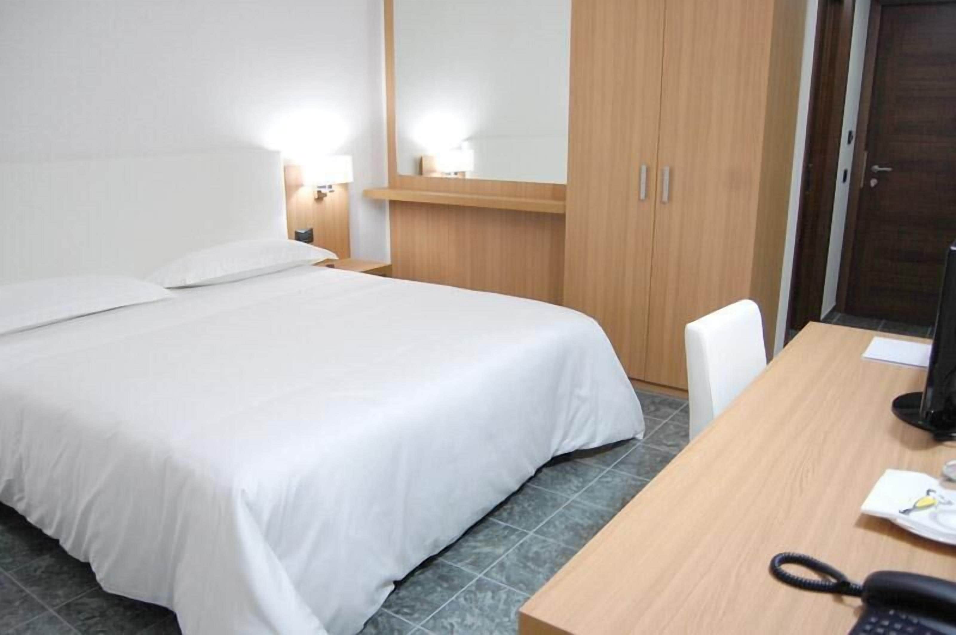 Una habitación de hotel con cama, escritorio, silla, teléfono y armario.