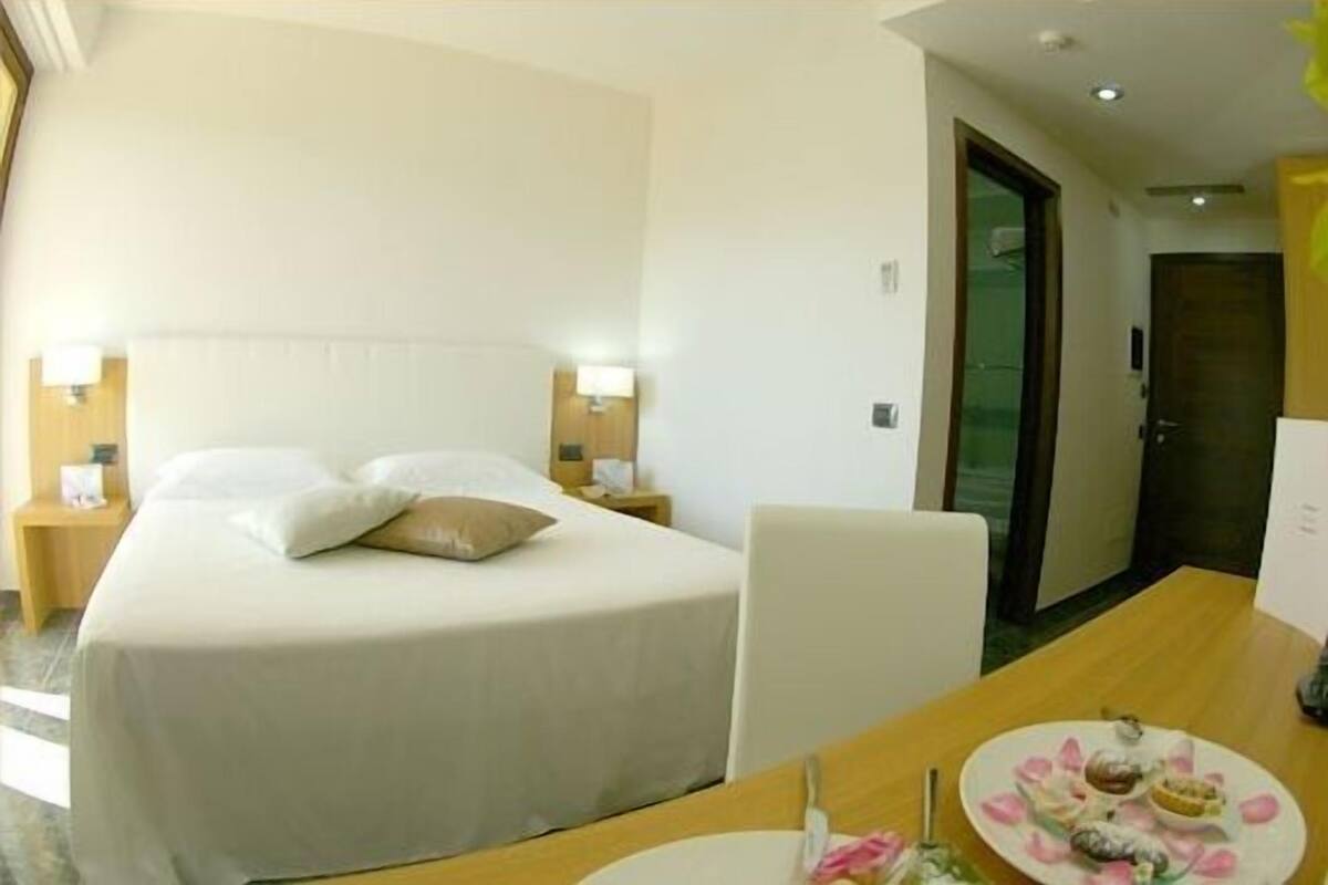 A hotel room with a bed, bedside tables, a wooden desk, and a plate of food.