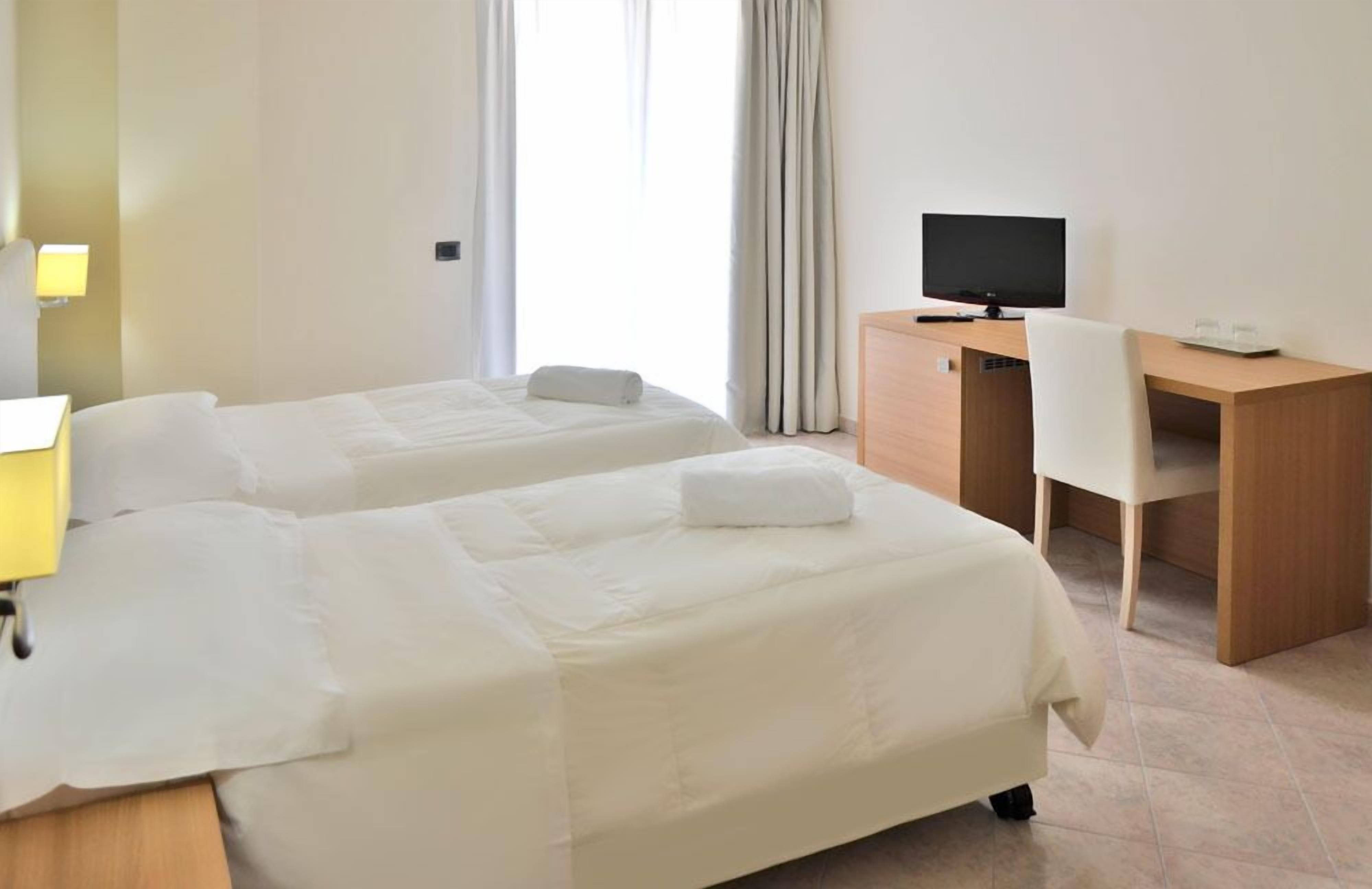 Una camera d'albergo con due letti, una scrivania, una sedia, una televisione e una lampada.