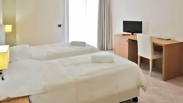 Una camera d'albergo con due letti, una scrivania, una sedia, una televisione e una lampada.