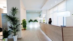 Un área de recepción moderna con un mostrador de madera, plantas en macetas y una persona de pie detrás del mostrador.