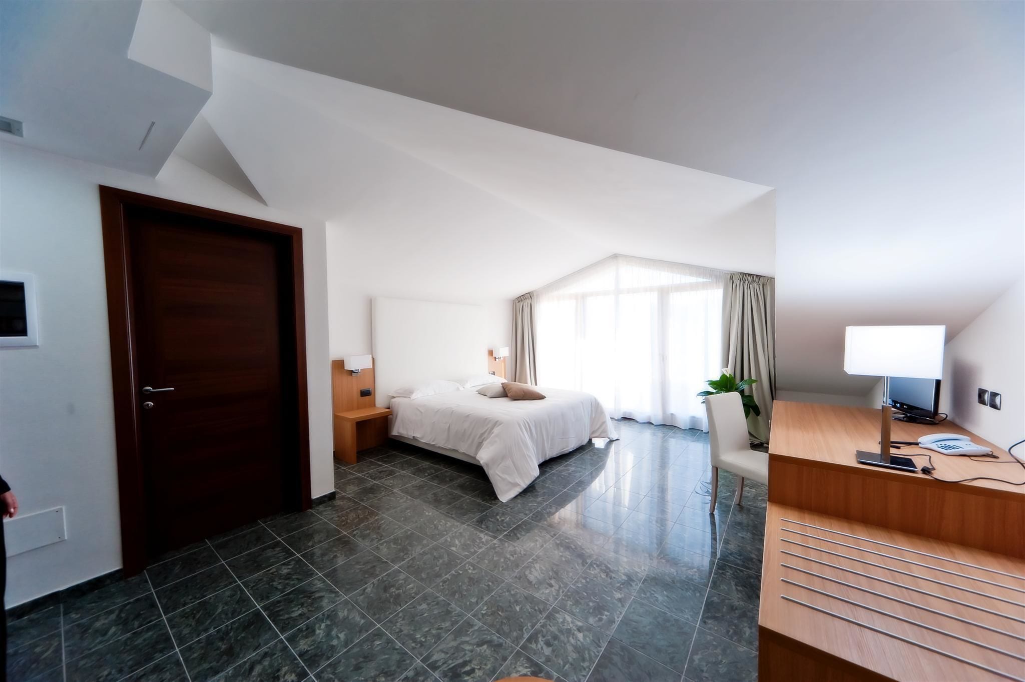 A modern hotel room with a bed, a desk, a chair, and a large window with curtains.