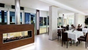Un comedor moderno con mesas dispuestas para los huéspedes, una chimenea central y grandes ventanales con vistas al exterior.