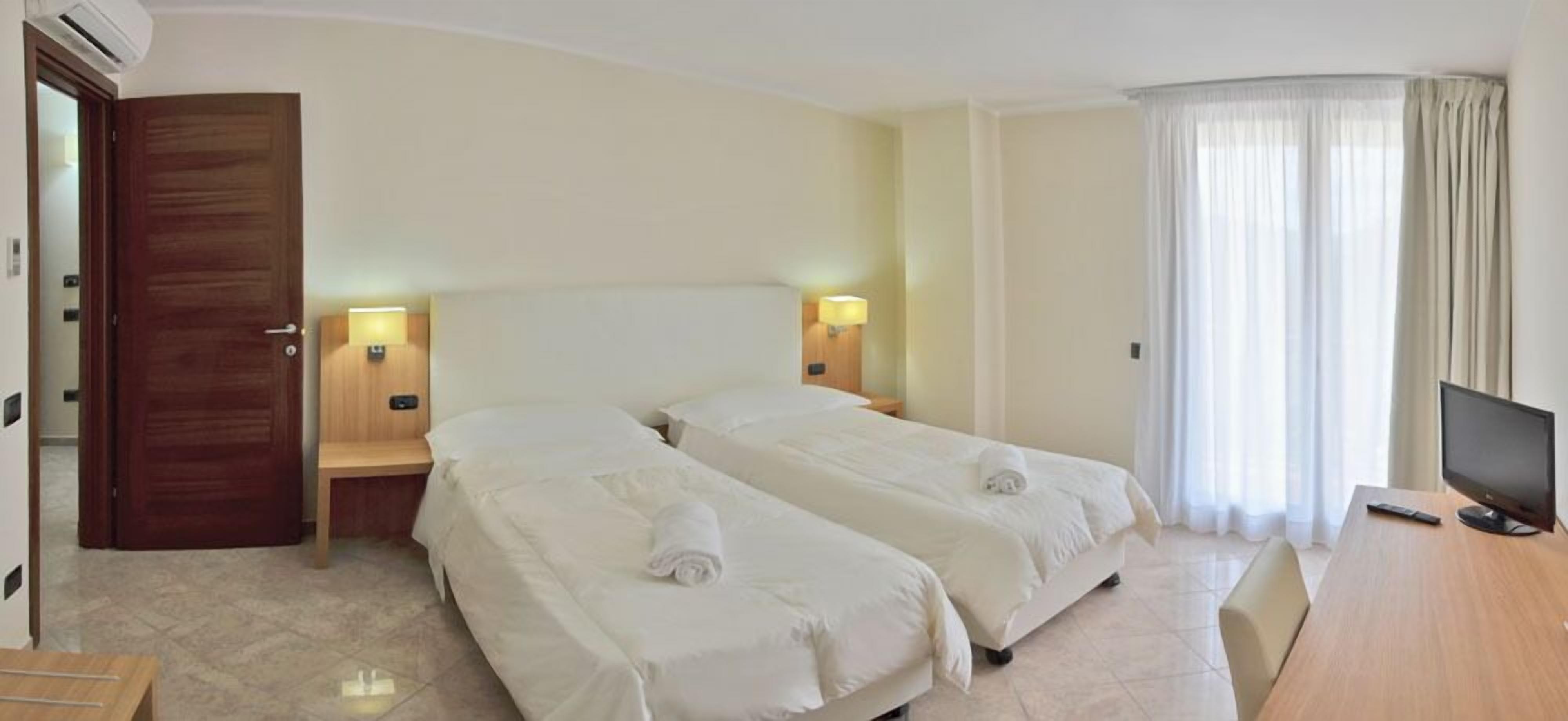 Una habitación de hotel con dos camas, televisión, escritorio y ventana con cortinas.