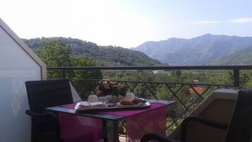 Enjoy a meal on the balcony with a serene mountain view, surrounded by lush greenery.