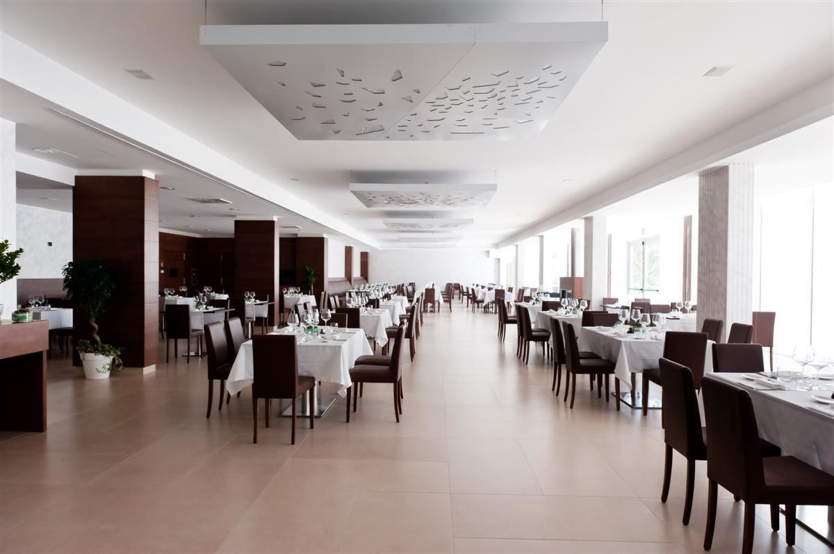 Un vaste espace dédié à la salle à manger, avec de nombreuses tables et chaises, de grandes fenêtres et un design moderne au niveau du plafond.