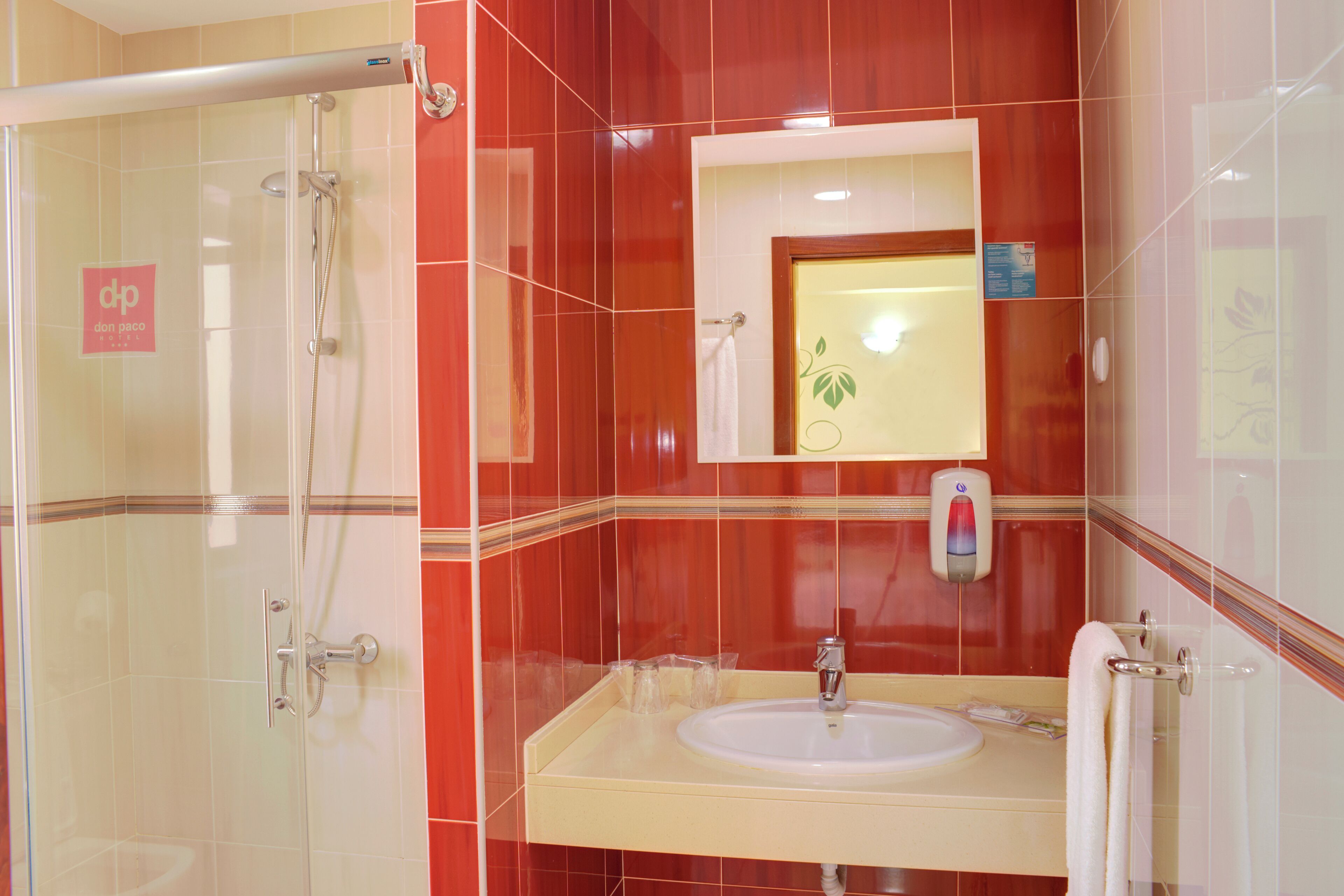 A bathroom with a glass shower enclosure, a sink with a mirror above it, and red-tiled walls.