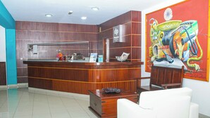 Una zona de recepció amb un taulell de fusta, un sofà blanc i un mural colorit a la paret.