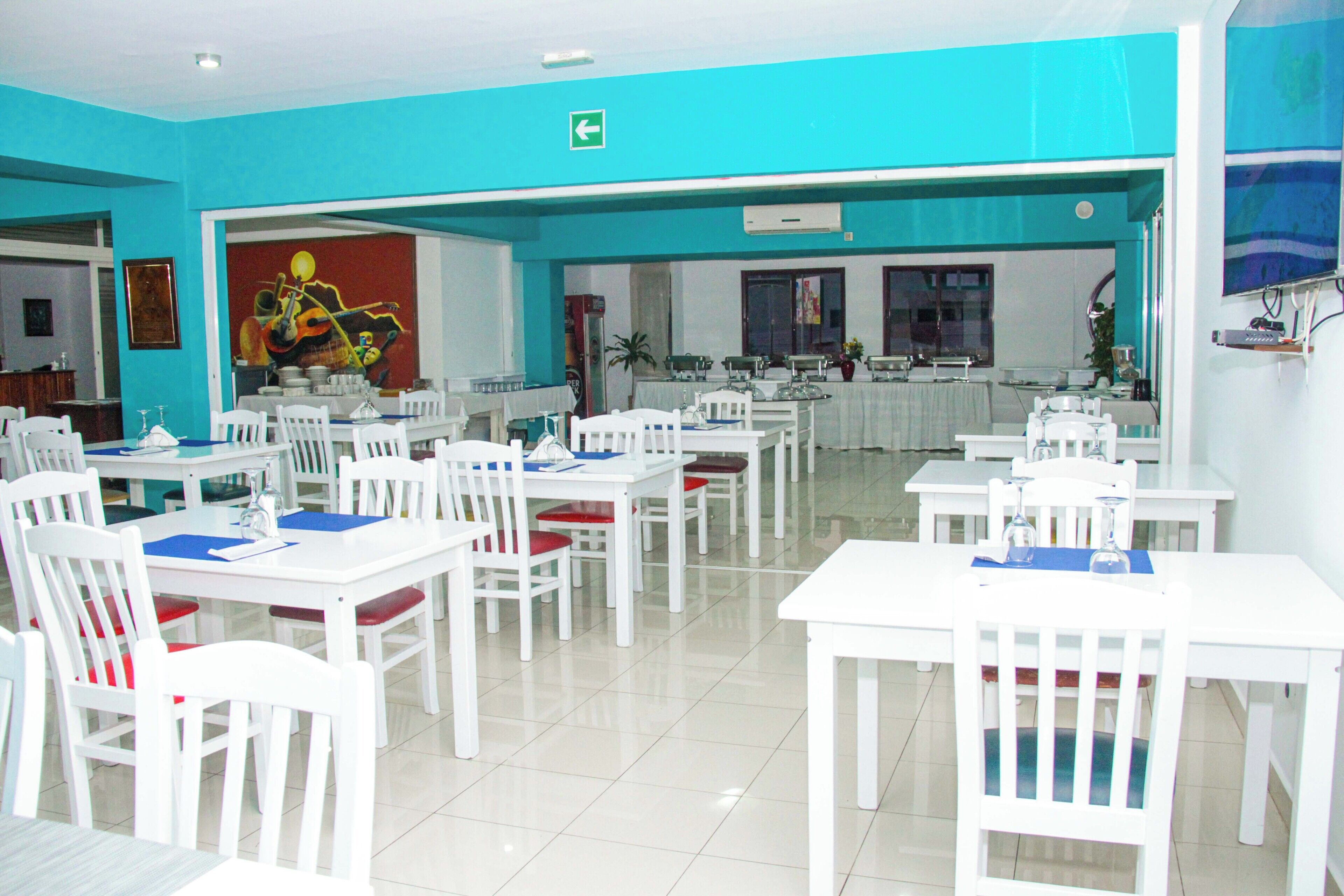 A dining area with white tables and chairs, a mural on the wall, and a blue accent wall.